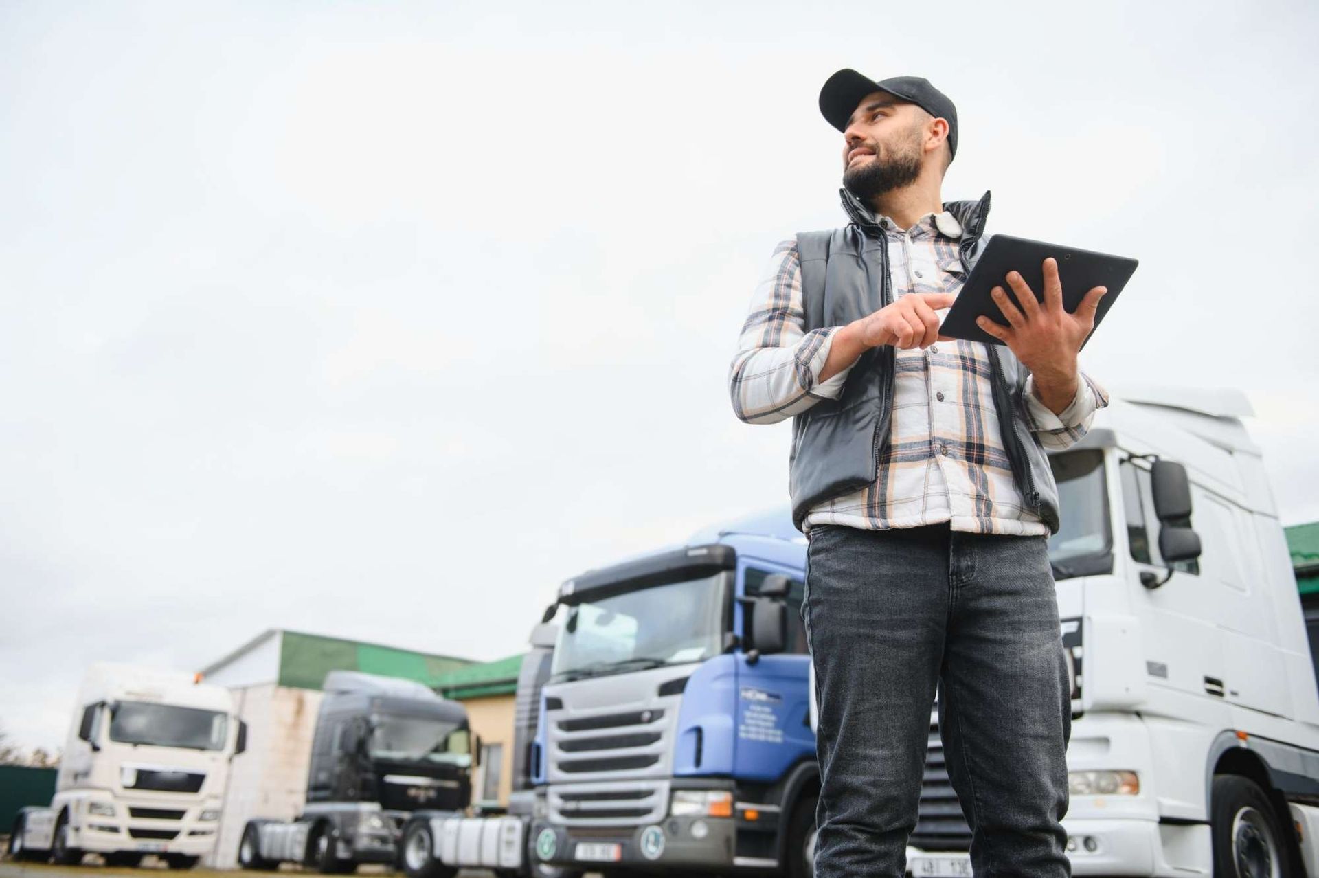LKW-Fahrer steht mit einem Tablet in einem Fuhrpark